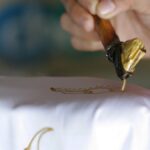 Perajin menorehkan malam dengan canting di atas kain batik tulis