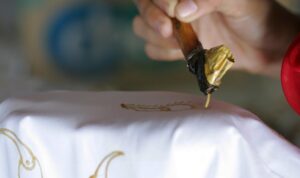 Perajin menorehkan malam dengan canting di atas kain batik tulis