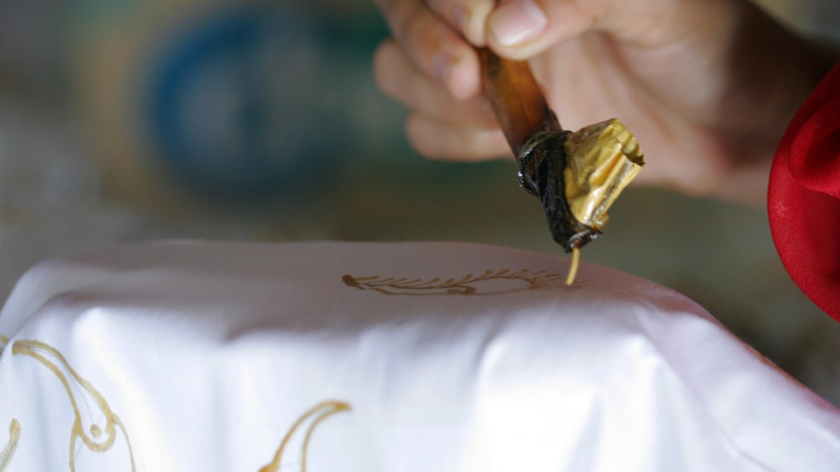 Perajin menorehkan malam dengan canting di atas kain batik tulis